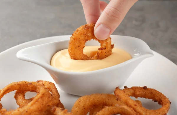 Woman dipping onion ring into gravy boat with sauce — Stock Photo, Image