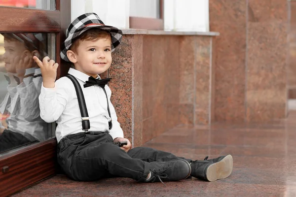 Schattige kleine jongen zitten in de buurt van gebouw ingang buiten — Stockfoto