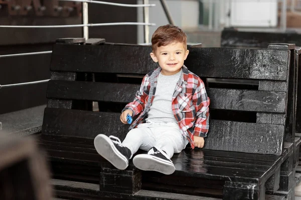 Чарівний маленький хлопчик сидить на лавці у відкритому кафе — стокове фото