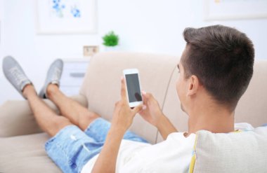 Genç adam evde kanepede Smartphone kullanarak