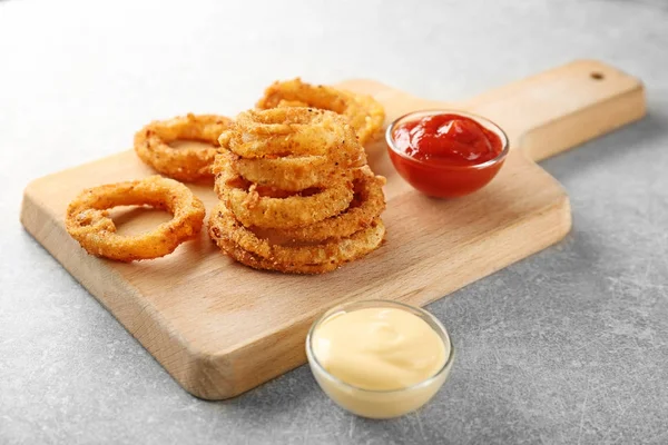 Tablero de madera con aros de cebolla frita y salsas — Foto de Stock