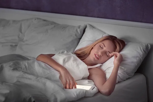 Bella giovane donna con telefono cellulare che dorme a letto — Foto Stock
