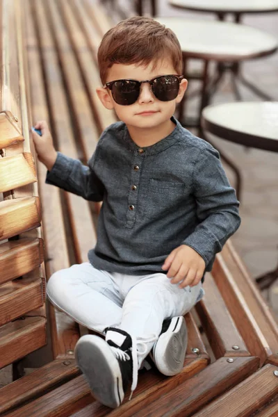 Adorable petit garçon assis sur le banc dans un café extérieur — Photo