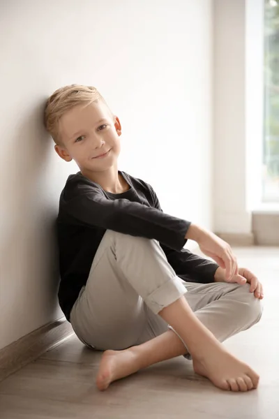 Lindo niño sentado cerca de la pared en casa —  Fotos de Stock