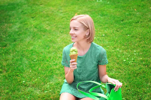 Fiatal, boldog csípő nő zöld csipke ruha gazdaság fagylalt ülve, a füves Park — Stock Fotó
