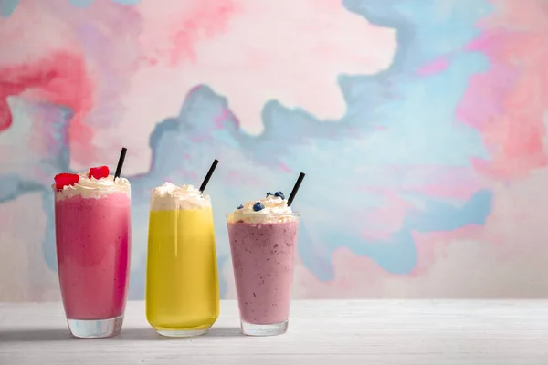 Διαφορετικές milkshakes σε ποτήρια στο τραπέζι κατά χρώμα φόντου — Φωτογραφία Αρχείου