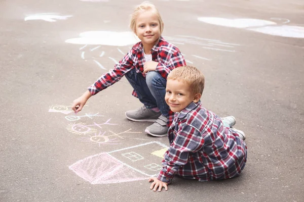Pequeños niños dibujando casa y familia con tiza sobre asfalto —  Fotos de Stock