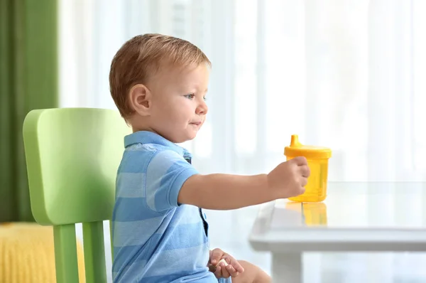 Adorable baby sitting at table with drinking bottle indoors — Stock Photo, Image