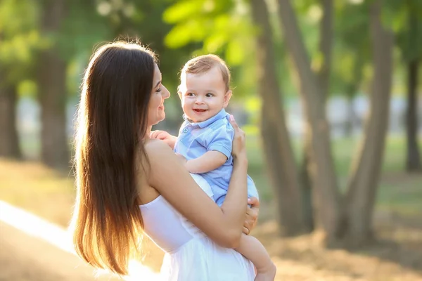 Schöne junge Mutter hält niedlichen Jungen im Freien — Stockfoto