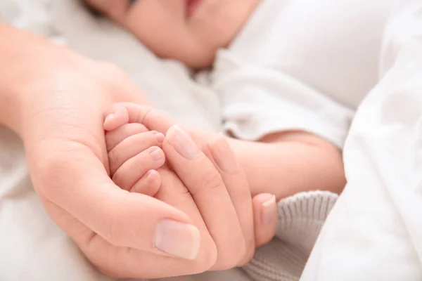 Baby holding mother 's hand on bed — стоковое фото