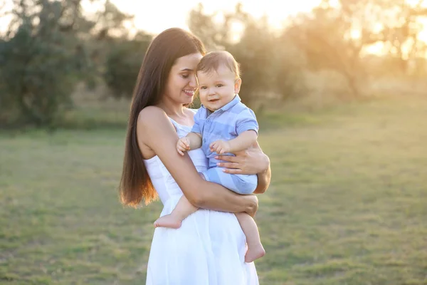 Hermosa madre joven sosteniendo lindo bebé niño, al aire libre —  Fotos de Stock