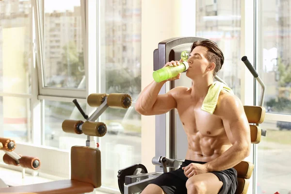 Muscular jovem bebendo água no ginásio — Fotografia de Stock