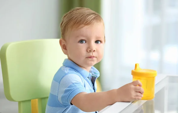 Schattig baby zit aan tafel met drinkfles binnenshuis — Stockfoto
