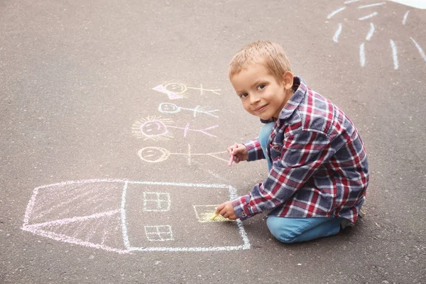 Little boy drawing house and family with chalk on asphalt