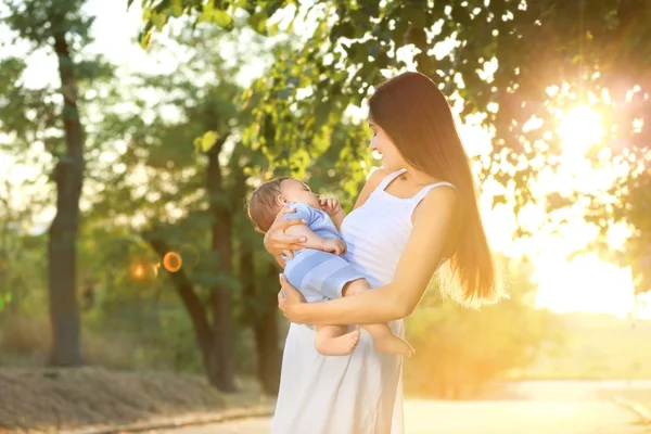 Schöne junge Mutter hält niedlichen Jungen im Freien — Stockfoto