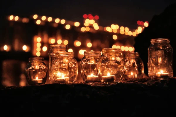 Frascos con velas encendidas en el fondo de luces borrosas por la noche — Foto de Stock