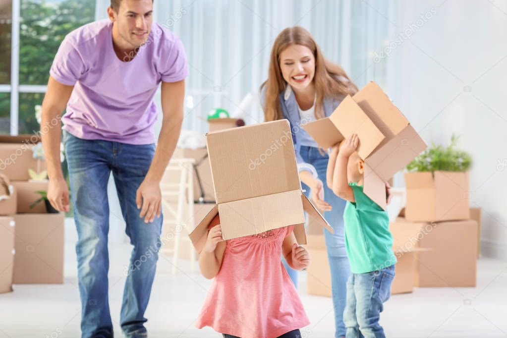 Young couple and cute little children playing with moving boxes in their new house