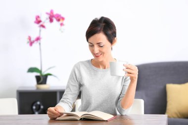 Evde kitap okuyan güzel olgun bir kadın.