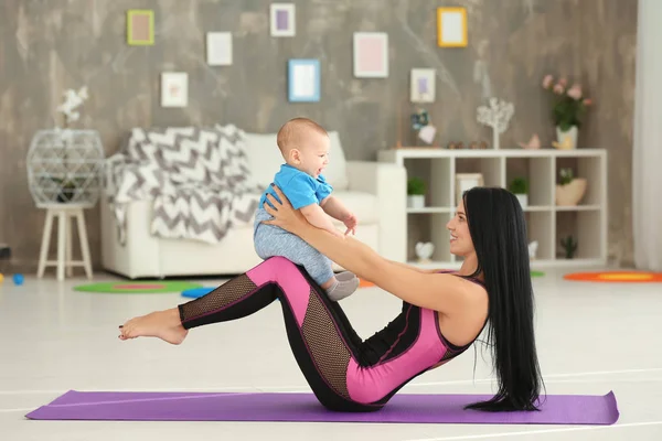 Jovem mãe fazendo exercícios enquanto segura o bebê em casa — Fotografia de Stock