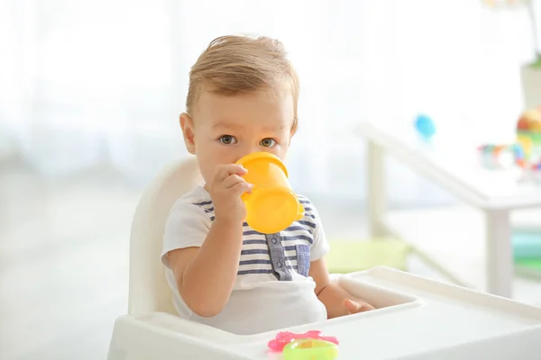 Bebê adorável bebendo de mamadeira enquanto sentado em cadeira alta em casa — Fotografia de Stock