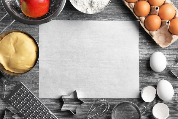 Пергаментная бумага и сырое тесто с ингредиентами на кухонном столе — стоковое фото