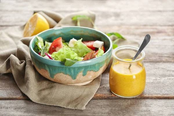 Bowl with salad and jar of tasty sauce — Stock Photo, Image