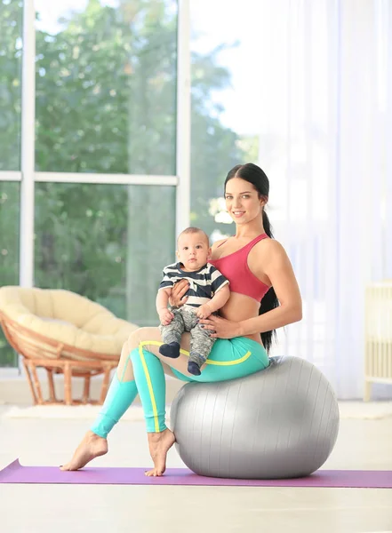 Jovem mãe fazendo exercícios enquanto segura o bebê em casa — Fotografia de Stock