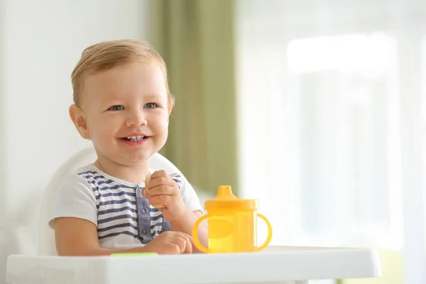 Adorable bebé comiendo manzana mientras está sentado en silla alta en casa —  Fotos de Stock