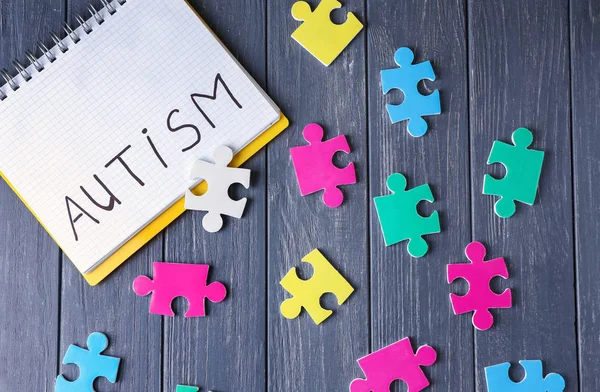 Parola AUTISMO scritto in taccuino e puzzle su sfondo di legno — Foto Stock