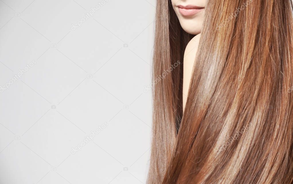 Young woman with beautiful long hair of caramel color on light background