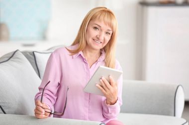 Güzel Olgun kadın evde koltukta oturan tablet bilgisayar ile