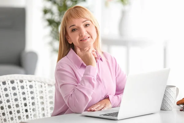 Mooie rijpe vrouw die op laptop thuis werkt — Stockfoto