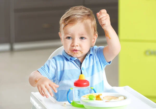 Adorable baby eating while sitting in highchair at home — Stock Photo, Image