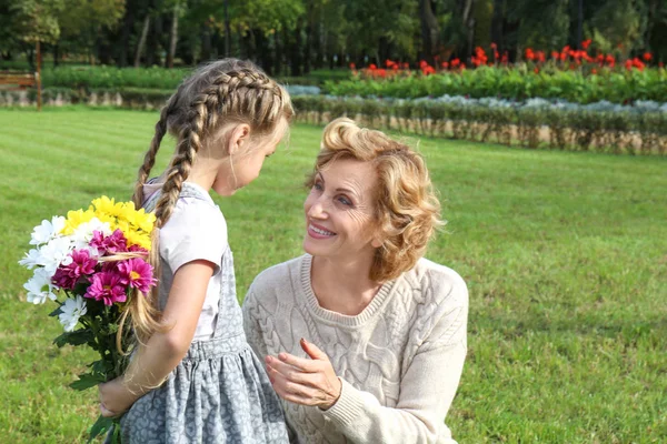 Schattig klein meisje boeket bloemen geven aan haar grootmoeder in park op zonnige dag — Stockfoto