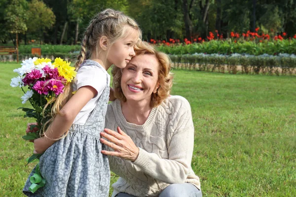 逗人喜爱的小女孩送花束给她的祖母在公园在晴朗的天 — 图库照片