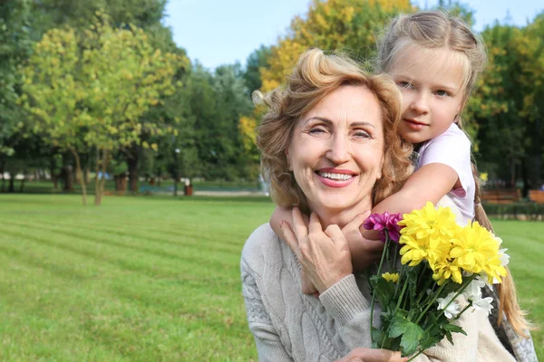 Linda niña y abuela con ramo de flores en el parque en el día soleado — Foto de Stock