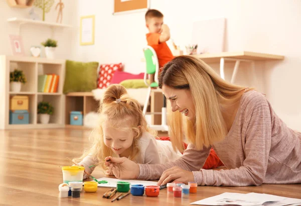 Mãe com foto bonito pintura menina na folha de papel, dentro de casa — Fotografia de Stock