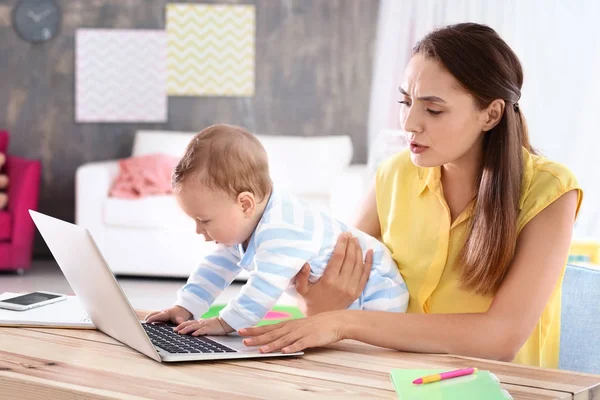 Ung mamma innehav baby medan du arbetar i hemmakontoret — Stockfoto