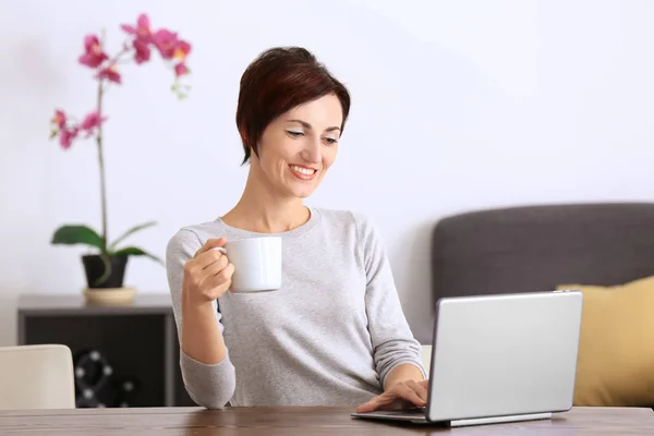 Schöne reife Frau mit Laptop und Kaffee zu Hause — Stockfoto