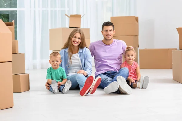 Gelukkige familie zittend op de vloer in de buurt van bewegende vakken in hun nieuwe huis — Stockfoto