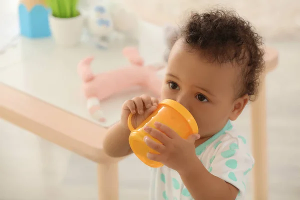 Schattige baby met flesje water binnenshuis — Stockfoto