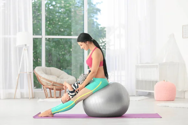 Jeune mère faisant des exercices tout en tenant bébé à la maison — Photo