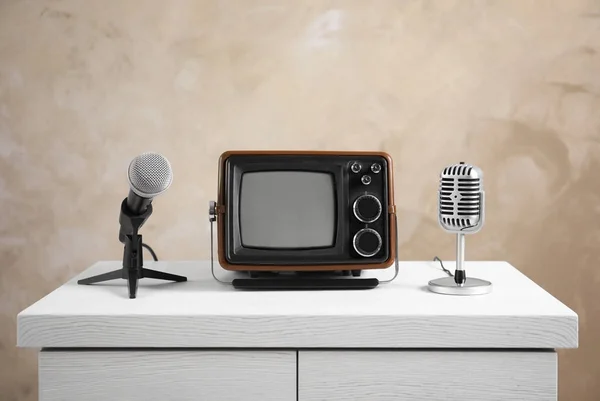 Retro draagbare Tv en microfoons op tafel tegen lichte muur — Stockfoto