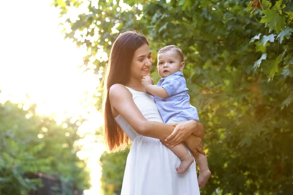 Schöne junge Mutter hält niedlichen Jungen im Freien — Stockfoto