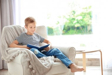 Sevimli küçük çocuk evde koltukta, okuma