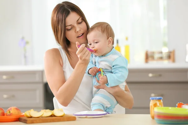 Mother feeding baby with spoon indoors — Stock Photo, Image