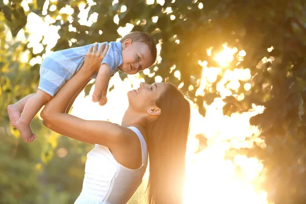 Schöne junge Mutter hält niedlichen Jungen im Freien — Stockfoto