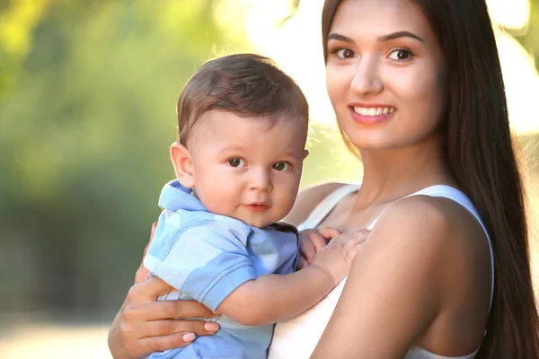 Ibu muda yang cantik menggendong bayi laki-laki lucu, di luar ruangan — Stok Foto
