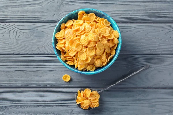 Schüssel und Löffel mit leckeren Cornflakes auf Holzgrund — Stockfoto