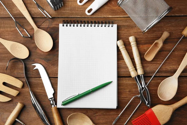 Cuaderno y varios utensilios de cocina sobre fondo de madera —  Fotos de Stock